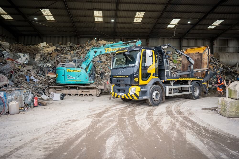 Towens skip lorry and excavator processing waste at a transfer station.